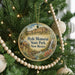 A round ornament hanging on a Christmas tree, featuring a scenic landscape with a waterfall and mountains.
