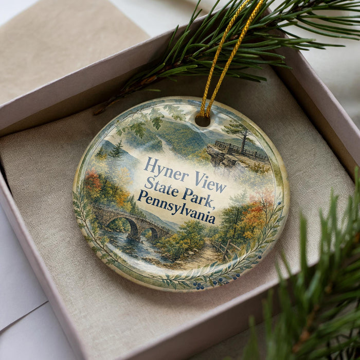 A decorative ornament in a box, featuring a scenic landscape with a bridge and trees, with the text "Hyner View State Park, Pennsylvania" printed on it.