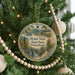 A round ornament hanging on a Christmas tree, featuring a scenic landscape with a bridge and mountains.
