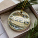 A decorative ornament in a box, featuring a scenic landscape of Iceland, including a castle, mountains, and water.