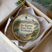 A decorative ornament in a box, featuring a scenic landscape with mountains, trees, and a lake.
