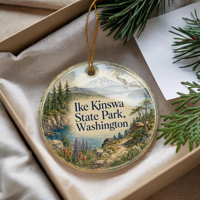 A decorative ornament with a scenic landscape of mountains, pine trees, and a body of water, hanging from a string.