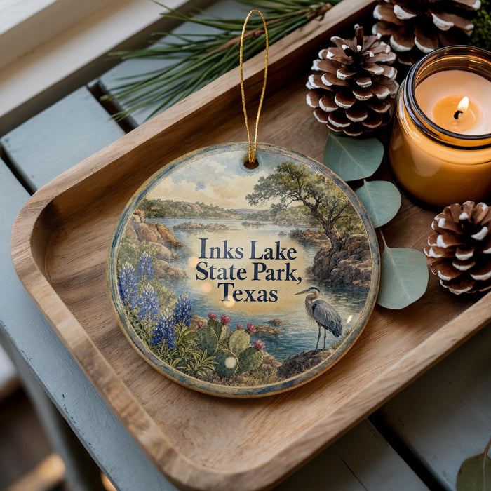 A decorative ornament with a scenic landscape of Inks Lake State Park, Texas, featuring a bird and surrounded by pine cones and a lit candle.