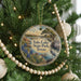 A circular ornament hanging on a Christmas tree, featuring a scenic landscape with a lake, mountains, and a bird.