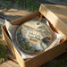 A circular ornament in a wooden box, featuring a scenic landscape with a lake, trees, and a bird, along with the text "Inks Lake State Park, Texas".
