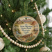 A round ornament hanging on a Christmas tree, featuring an illustration of a historic building and landscape.