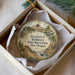 A round ornament in a white box, featuring a scenic landscape with a house, a bird, and a sailboat.