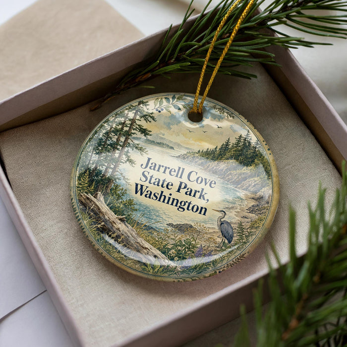 A decorative ornament with a scenic landscape of trees, water, and a bird is displayed in a box, surrounded by pine branches.