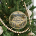 A Christmas tree ornament with a scenic landscape of a mountain, river, and cabin, surrounded by pine trees and beaded decorations.