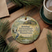 A round ornament with a bird perched on a branch, surrounded by greenery, sits on a wooden surface.