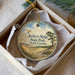 A round ornament with a scenic landscape and a bird in flight, placed in a white box with a gold string.
