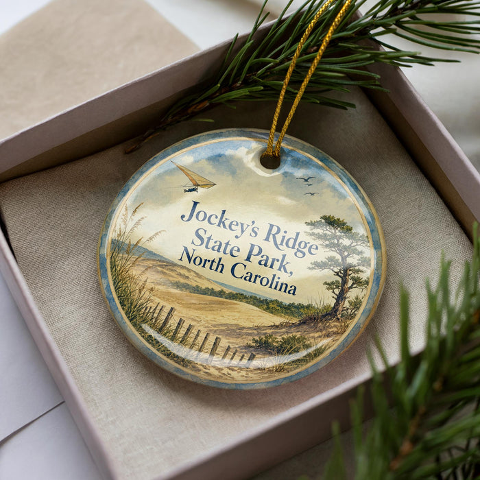 A decorative ornament in a box, featuring a scenic landscape with a beach, trees, and a bird in flight.