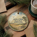 A round ornament with a scenic landscape of Jockey's Ridge State Park, North Carolina, featuring a bird flying over a field and a tree.