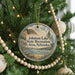 A round ornament hanging on a Christmas tree, featuring a scenic landscape with a lake, mountains, and trees.