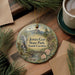 A round ornament with a scenic landscape of Jones Gap State Park, South Carolina, featuring a mountain, waterfall, and pine trees.