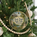 A round ornament hanging on a Christmas tree, featuring a scenic image of a trail and a bridge.