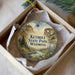 A decorative ornament in a box, featuring a scenic landscape with mountains, trees, and a lake.
