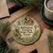 A circular ornament with the text "Kickapoo Cave State Park, Texas" is displayed on a wooden surface, surrounded by pine branches and a cup of coffee.