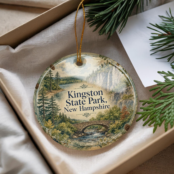 A decorative ornament with a scenic landscape of Kingston State Park, New Hampshire, featuring a bridge and pine trees.