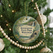 A circular ornament hanging on a Christmas tree, featuring a scenic landscape with a waterfall and trees.