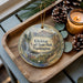 A decorative ornament with a scenic mountain landscape and a waterfall, featuring the text "Klickitat Trail State Park, Washington". The ornament is placed on a wooden tray, with pine cones and a lit candle nearby.