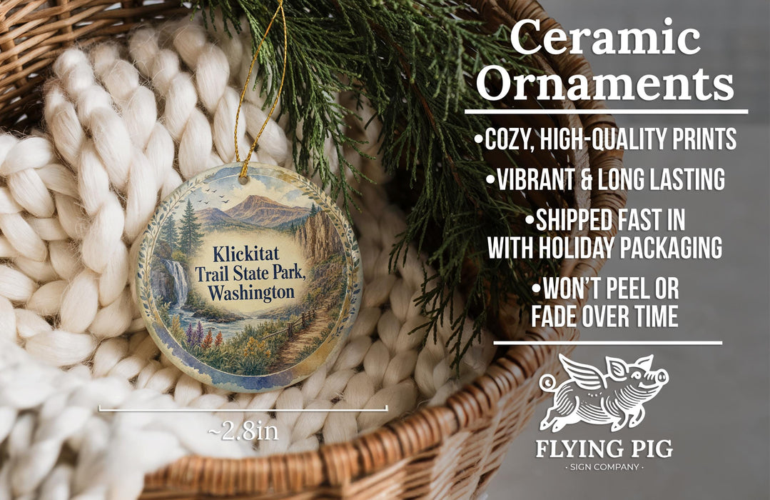 Ceramic ornaments, specifically those shaped like the Klickitat Trail State Park in Washington, are displayed in a woven basket. The ornaments are described as cozy, high-quality prints, vibrant, and long-lasting, and are shipped fast in holiday packaging. They are not to be peeled or faded over time. The image also includes a logo for the Flying Pig Sign Company.