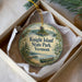 A decorative ornament in a box, featuring a scenic landscape with a lake, mountains, and pine trees.