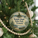 A round ornament hanging on a Christmas tree, featuring a scenic image of a lake and mountains with a boat in the foreground.