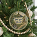 A round ornament hanging on a Christmas tree, featuring a scenic landscape with a bridge and a lake.