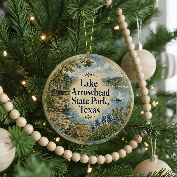 A round ornament hanging on a Christmas tree, featuring a scenic landscape with a lake, trees, and a sailboat.