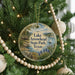 A round ornament hanging on a Christmas tree, featuring a scenic landscape with a lake, trees, and a sailboat.