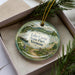 A decorative ornament with a scenic landscape of Lake Carmi State Park, Vermont, featuring a path, trees, and mountains.