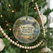 A round ornament hanging on a Christmas tree, featuring a scenic landscape with mountains, a lake, and a boat.