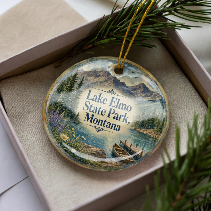 A decorative ornament in a box, featuring a scenic landscape with mountains, water, and pine trees.
