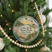 A round ornament hanging on a Christmas tree, featuring a lighthouse and a beach scene.
