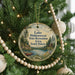A round ornament hanging on a Christmas tree, featuring a scenic landscape with a lake, trees, and a cabin.