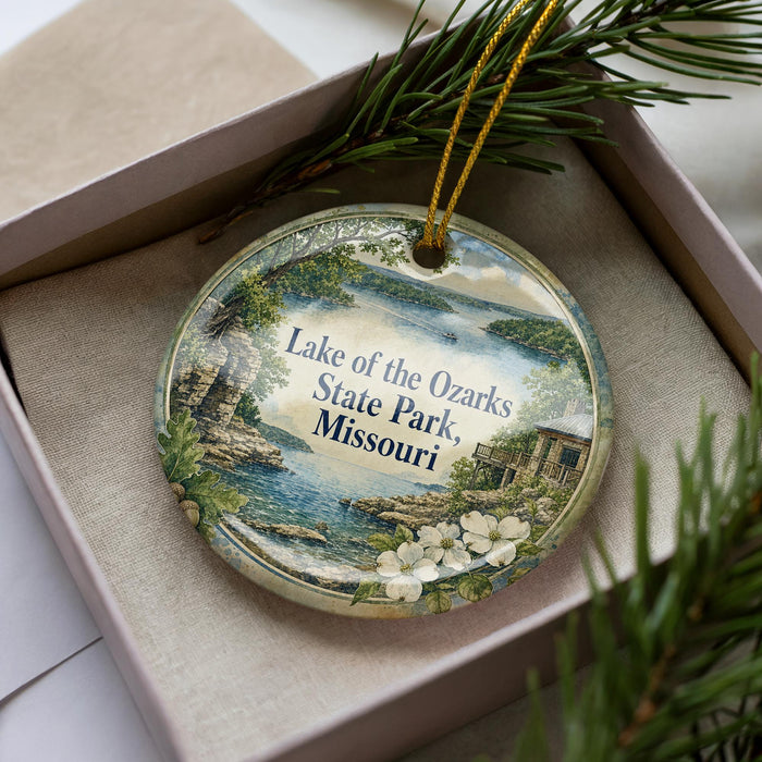A decorative ornament with a lake scene and text, placed in a box with pine branches.