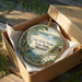 A decorative ornament in a box, featuring a scenic landscape with a lake and trees, with the text "Lake of the Ozarks State Park, Missouri" printed on it.