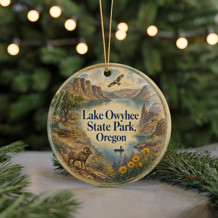 A round ornament with a scenic landscape of Lake Owyhee State Park, Oregon, featuring a mountain range, a lake, and various wildlife.