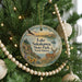 A round ornament hanging on a Christmas tree, featuring a scenic landscape with a lake, a deer, and mountains in the background.