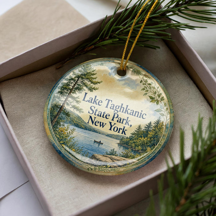 A decorative ornament with a scenic lake and forest landscape, featuring a boat on the water, is displayed in a box with pine branches.