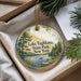 A round ornament with a scenic lake and forest landscape, hanging from a string.
