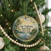 A round ornament hanging on a Christmas tree, featuring a scenic landscape with a lake and pine trees.