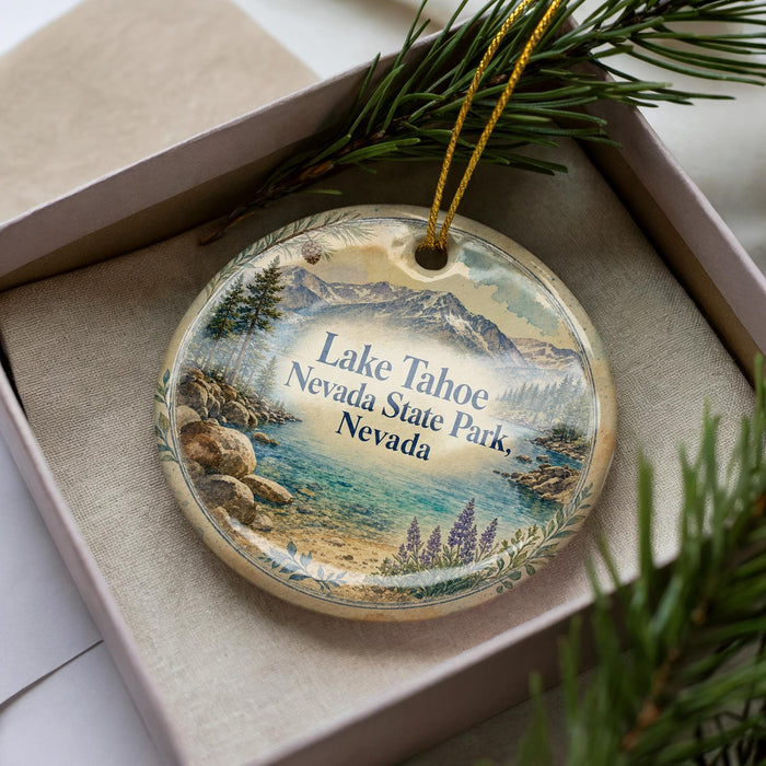 A decorative ornament with a landscape scene featuring Lake Tahoe, Nevada, is displayed in a box with pine branches.