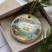 A decorative ornament with a landscape scene featuring Lake Tahoe, Nevada, is displayed in a box with pine branches.