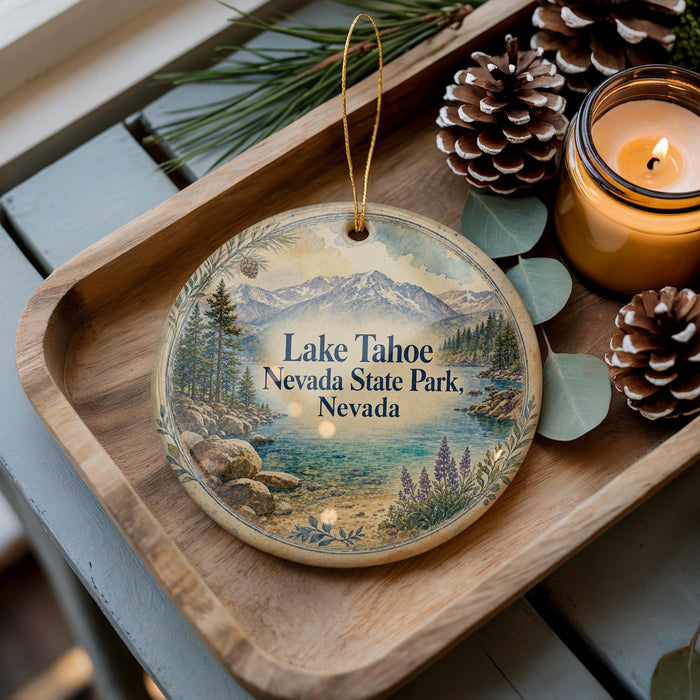 A decorative ornament with a scenic image of Lake Tahoe, Nevada, featuring mountains, pine trees, and a lake, is displayed on a wooden tray alongside pine cones and a lit candle.