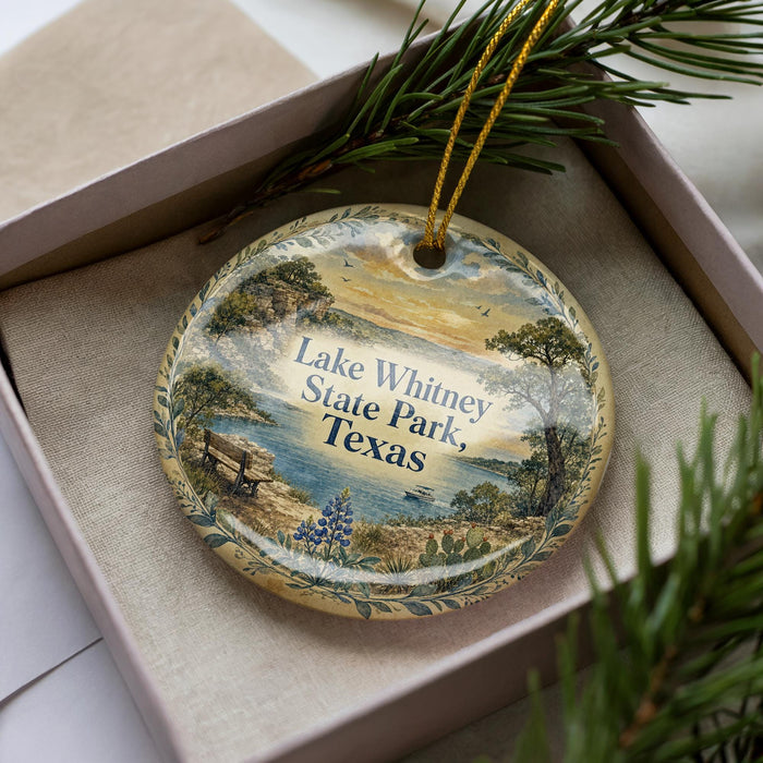 A decorative ornament in a box, featuring a scenic landscape with a lake, trees, and a sunset.