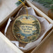 A decorative ornament in a white box, featuring a scenic landscape with a lake, trees, and a bench.