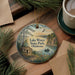 A round ornament with a painting of Lake Wister State Park, Oklahoma, featuring a cabin, a river, and a bird in flight.