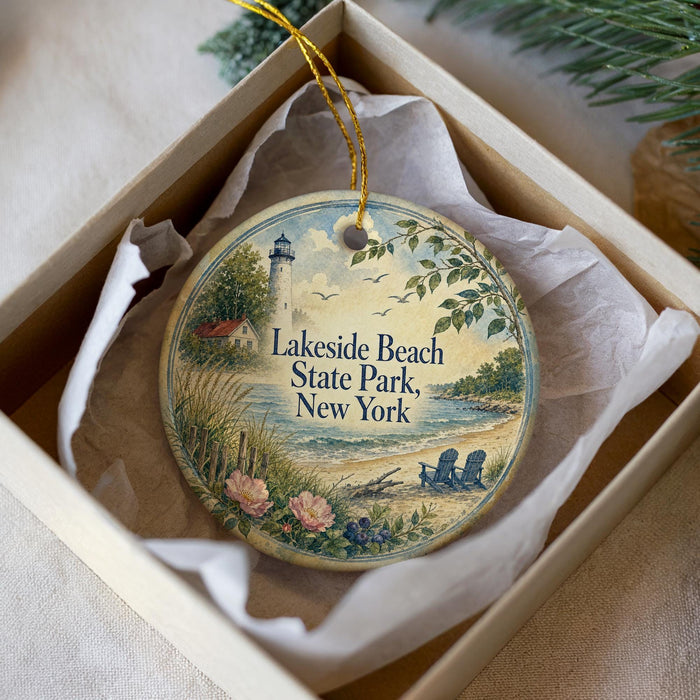 A decorative ornament in a box, featuring a lighthouse and a beach scene with a couple of chairs.